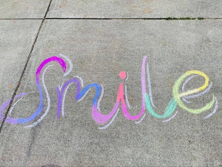 the word smile written in colored chalk on concrete with sidewalk marking it's name