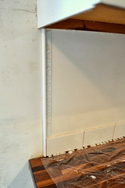 a cat sitting on top of a wooden floor next to a white wall and wood shelf