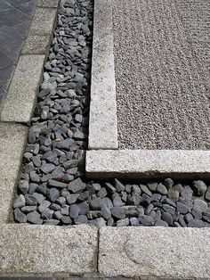 a stone bench sitting next to a graveled area with rocks on the ground and grass growing in between it