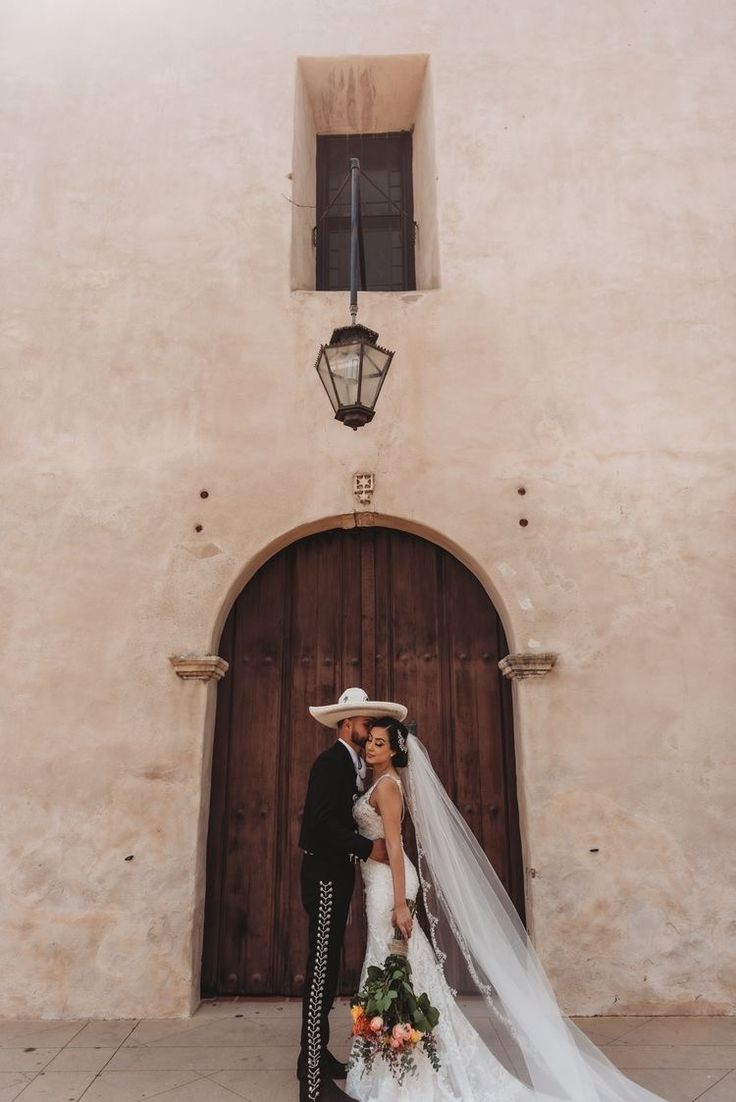 a bride and groom standing in front of a building with a light fixture on the side