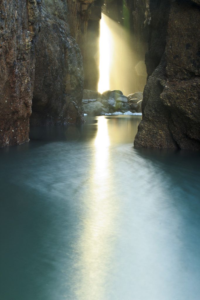 the sun shines brightly through an opening in a rock formation over a body of water