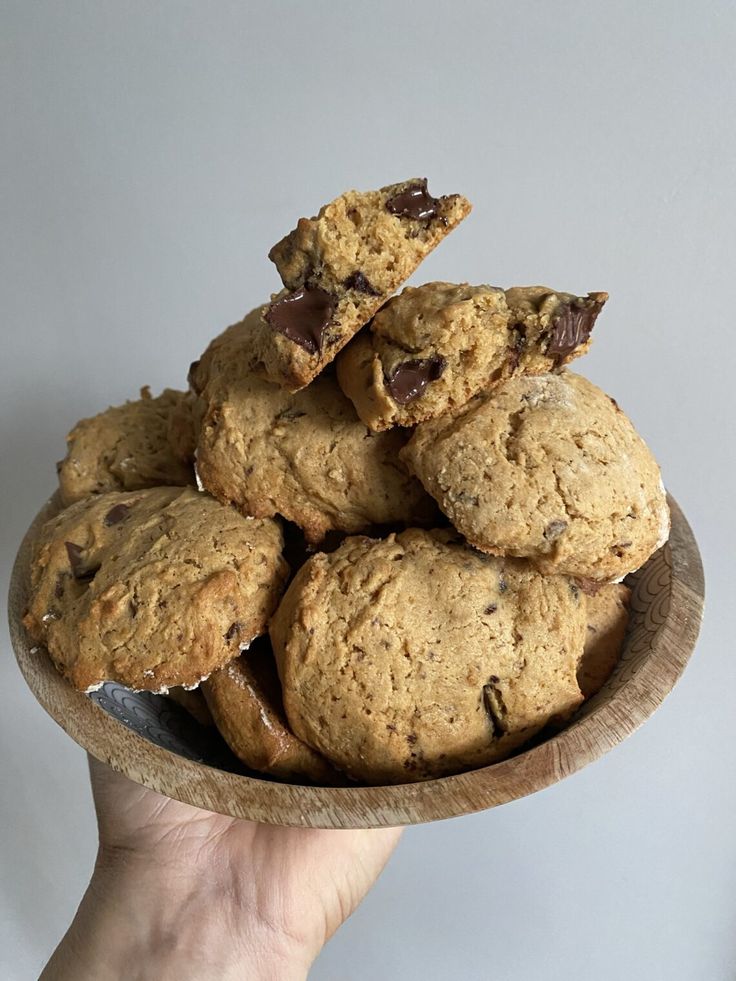 a hand holding a bowl full of cookies with chocolate chips on top and in the middle