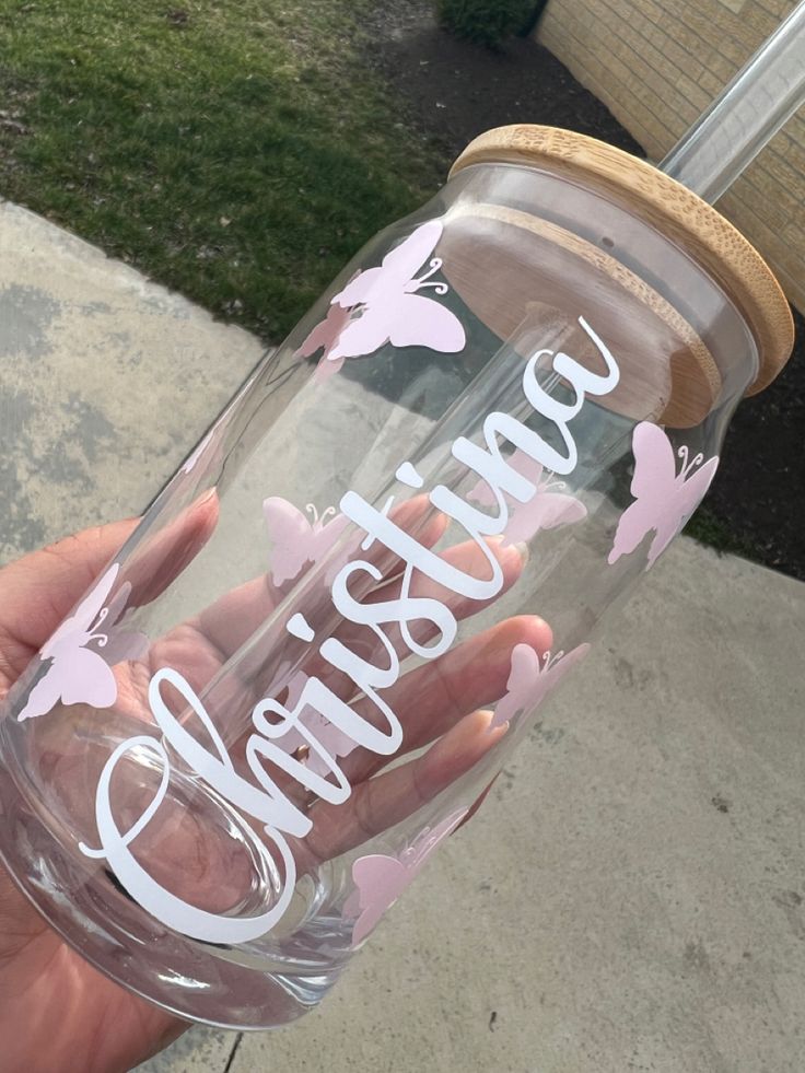 a person holding up a clear cup with pink butterflies on it and the words grandma written in white