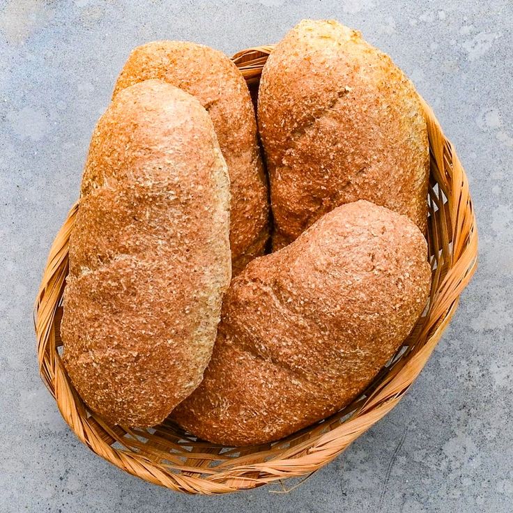 four loaves of bread in a wicker basket on a concrete surface, top view