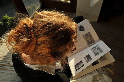 a woman with red hair sitting on top of a bed next to an open book