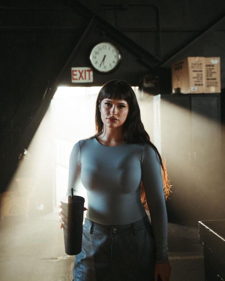 a woman holding a cup standing in front of a clock