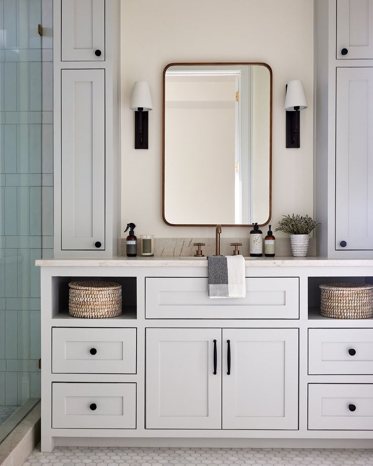 a white bathroom with two sinks and a large mirror above the sink is surrounded by cabinetry