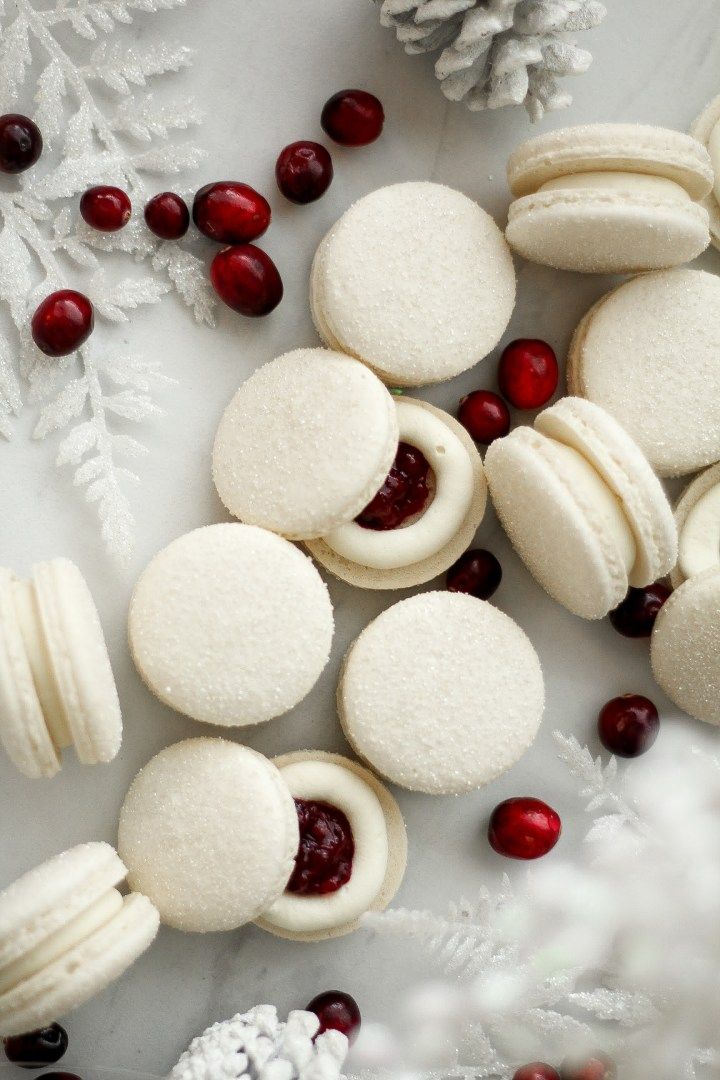 white macaroons with cranberry filling on a plate next to snowflakes