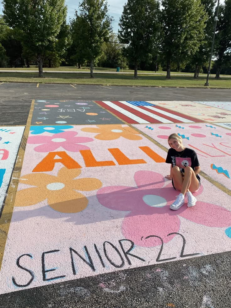 a woman kneeling on the ground in front of a painted parking lot with words all senior 22