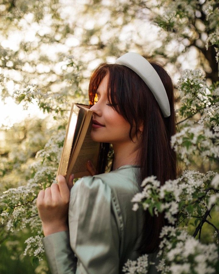 a woman is standing in the woods holding a book and looking into the distance with her eyes closed