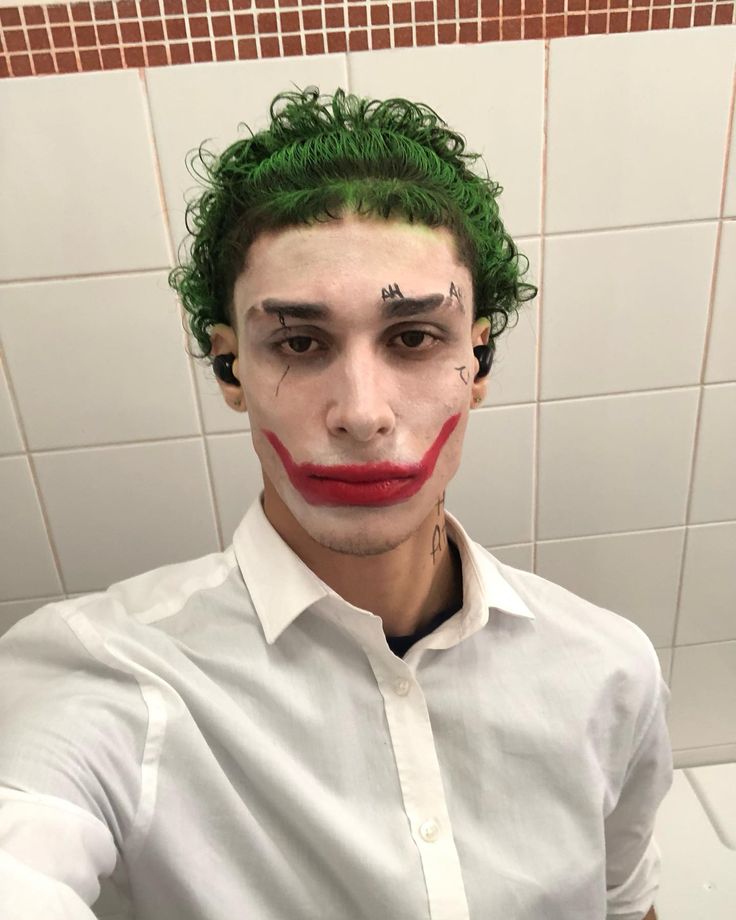 a man with green hair and clown make up in a bathroom wearing a white shirt