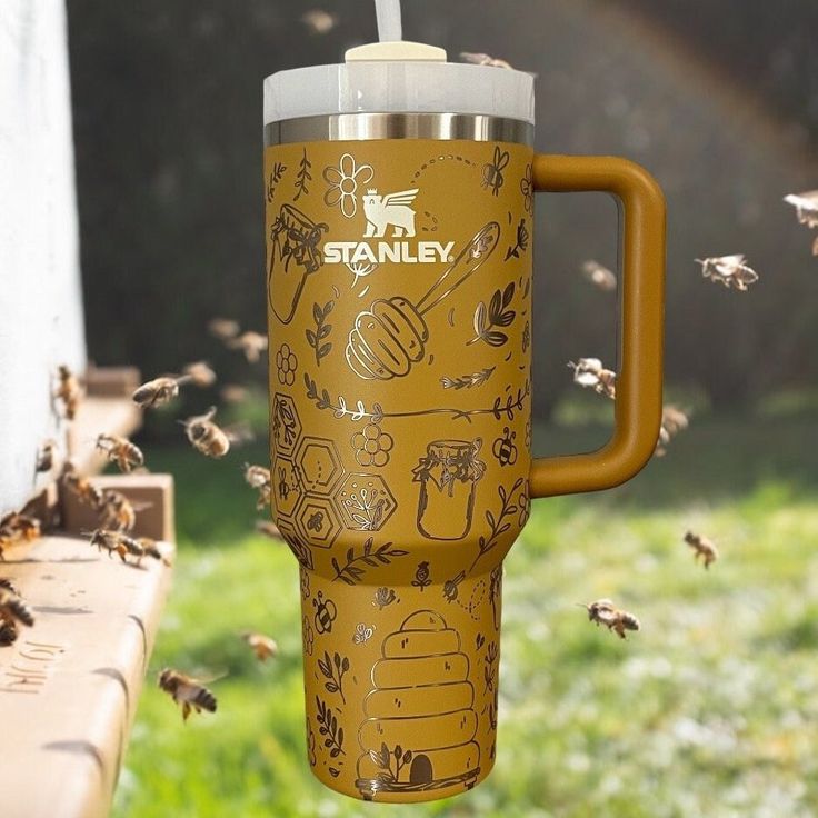 a yellow travel mug sitting on top of a wooden bench next to bees flying around