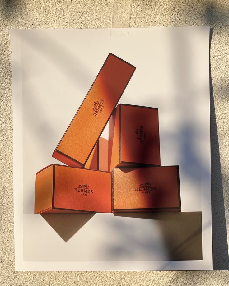 four orange boxes sitting on top of each other in front of a white wall and shadow