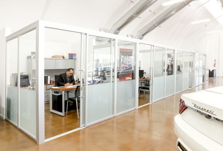 a man sitting at a desk in an office with glass partitions on the walls