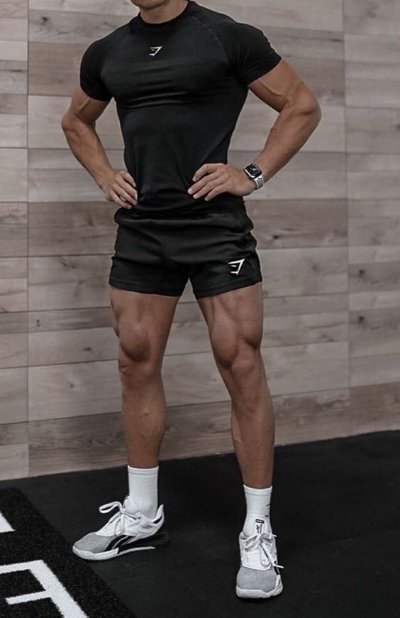 a man standing in front of a wooden wall with his hands on his hips wearing black shorts