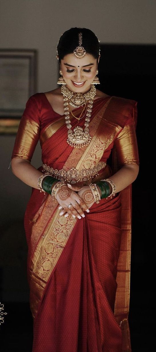 a woman in a red and gold sari with jewelry on her neck, smiling at the camera