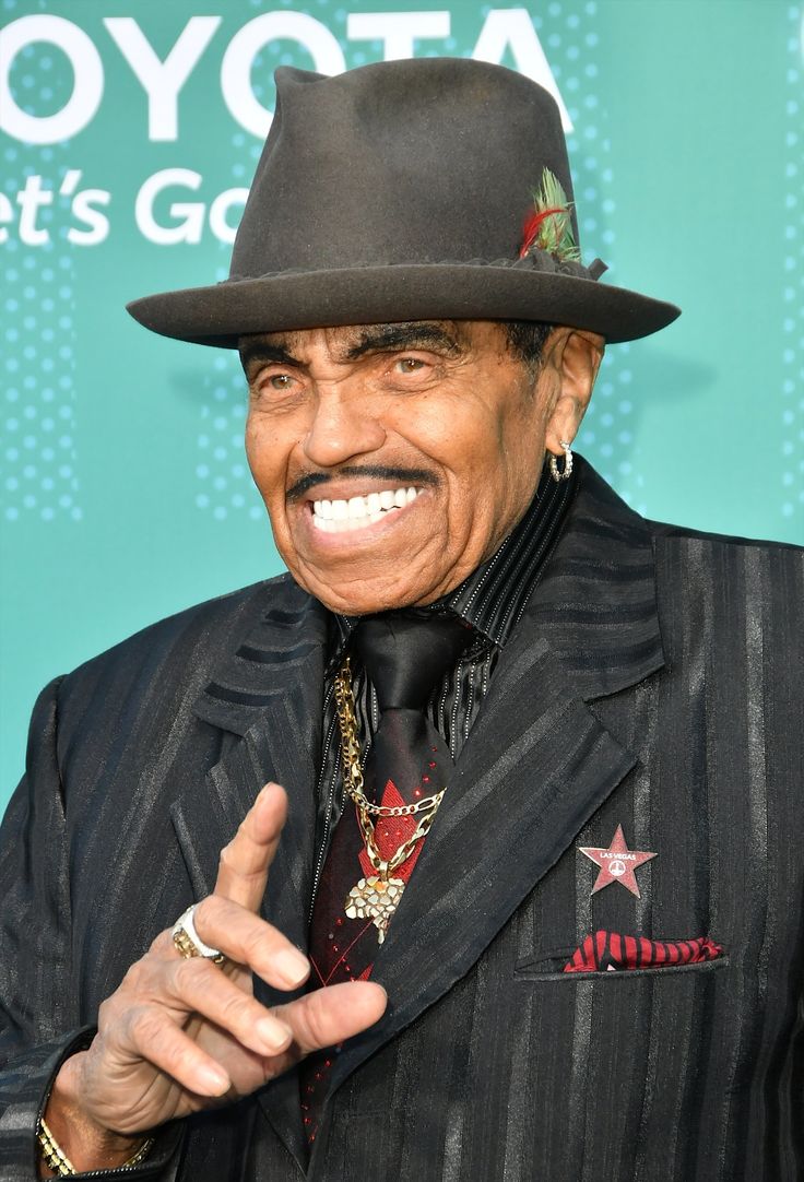 an older man in a suit and hat giving the peace sign with his right hand