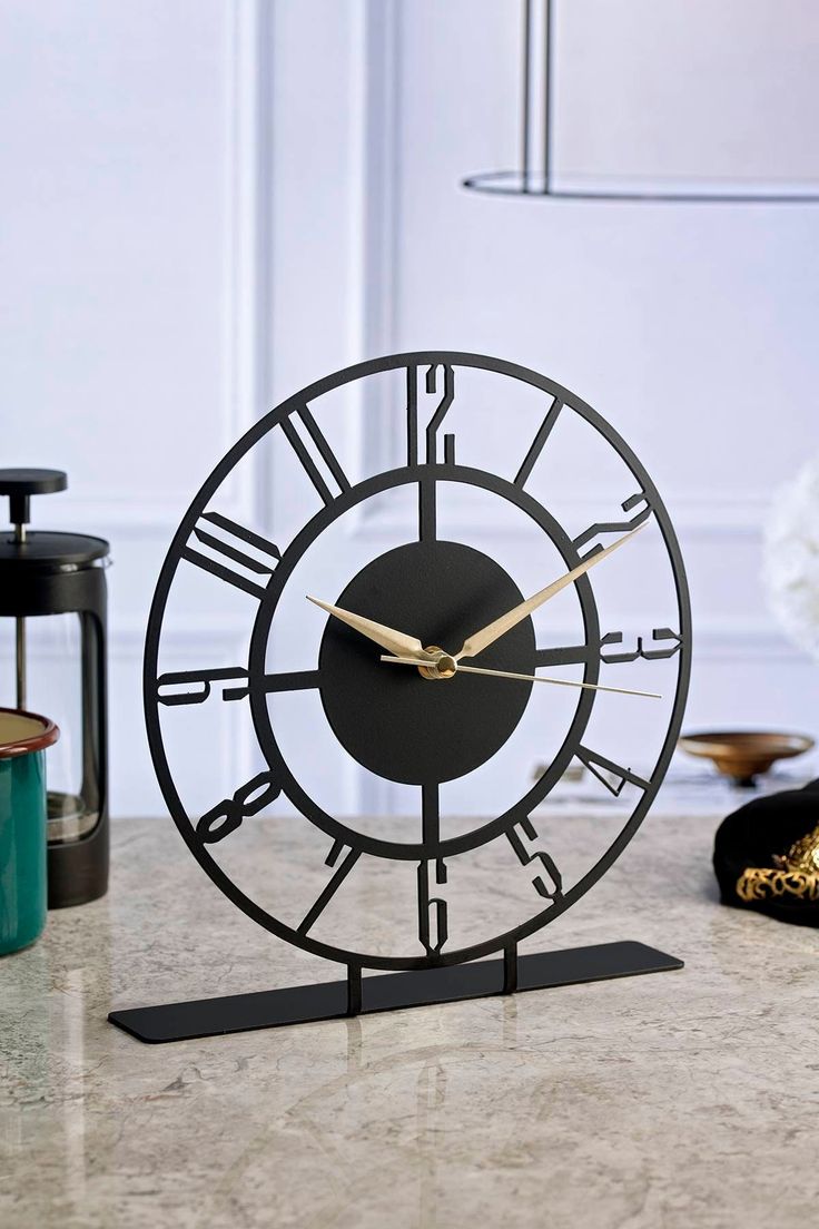 a black clock sitting on top of a table next to a vase and candle holder