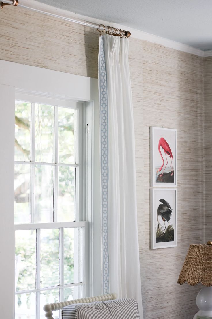 a living room filled with furniture and windows covered in white drapes next to a lamp