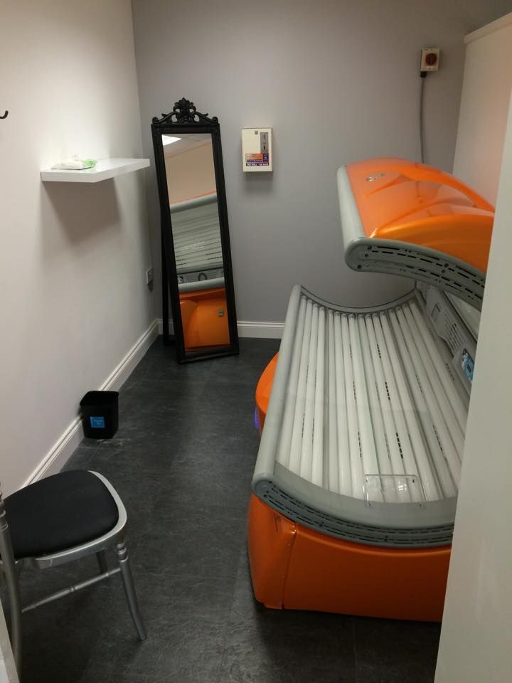 an orange and white bed in a room next to a black chair with a mirror on the wall