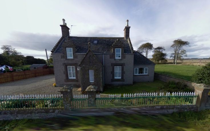 an aerial view of a house with a fence in the foreground and green grass on the other side