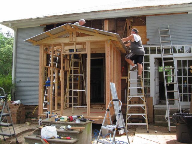 a man standing on top of a ladder next to a house under construction with windows