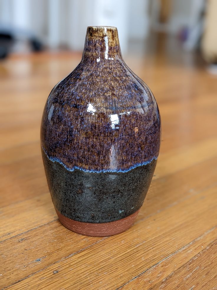 a brown and black vase sitting on top of a wooden table