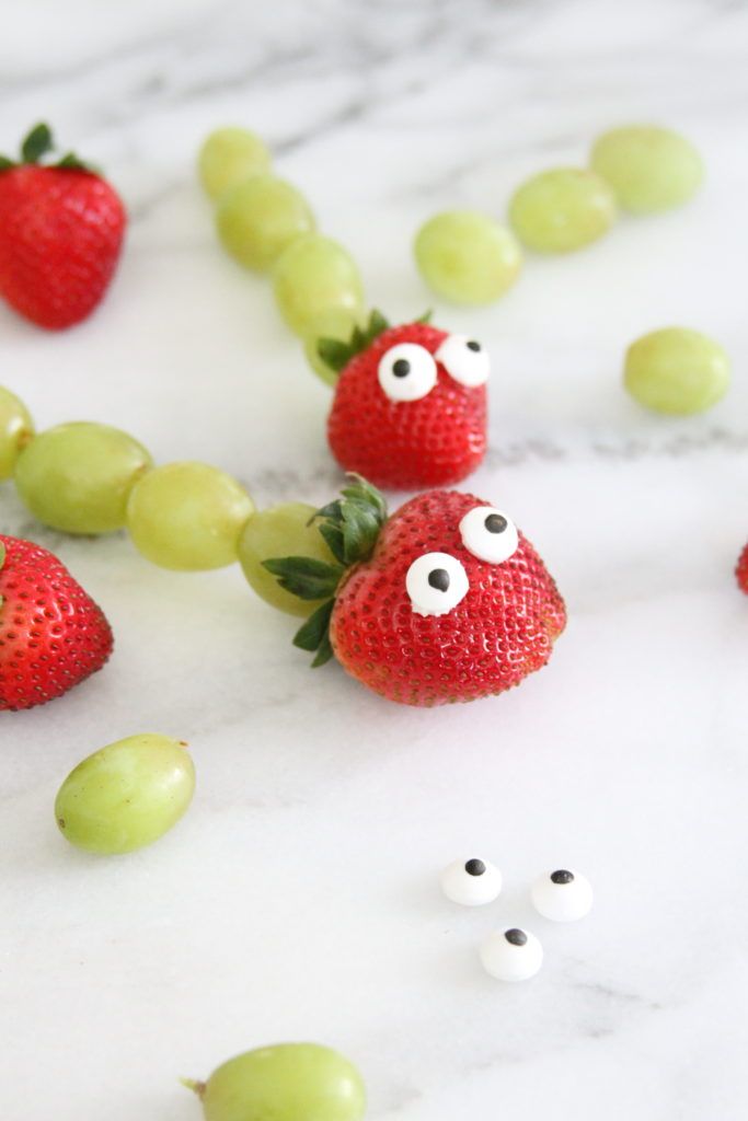 strawberries and grapes with googly eyes are on the marble countertop next to green grapes