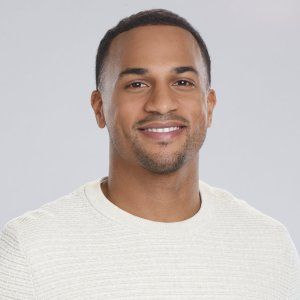 a close up of a person wearing a white sweater and smiling at the camera with a gray background