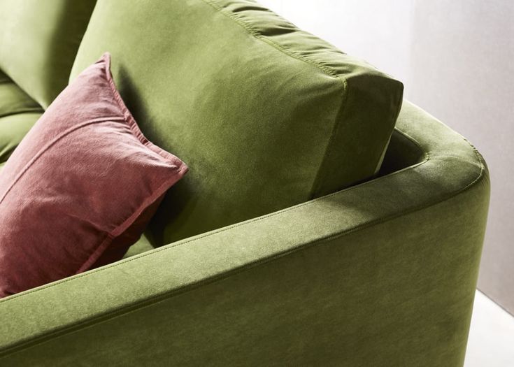 a green couch with two red pillows on it's back and one pink pillow