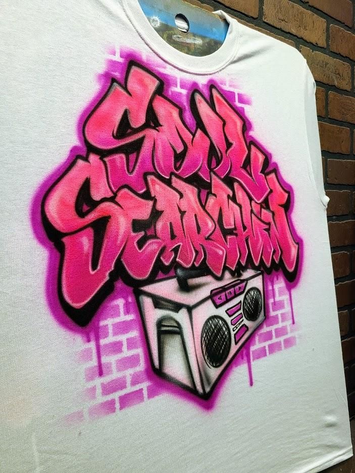 a white t - shirt with pink graffiti on the front and back, against a brick wall