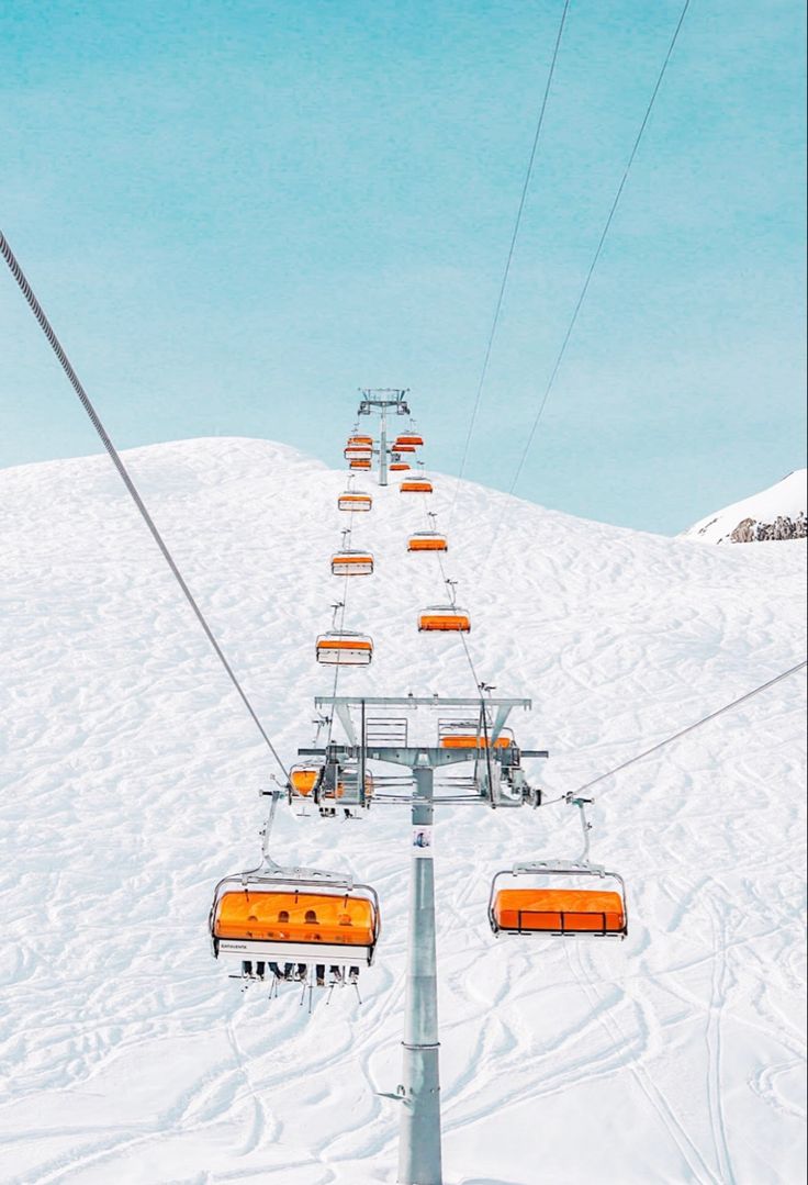 a ski lift going up the side of a snow covered mountain with orange chairs on it