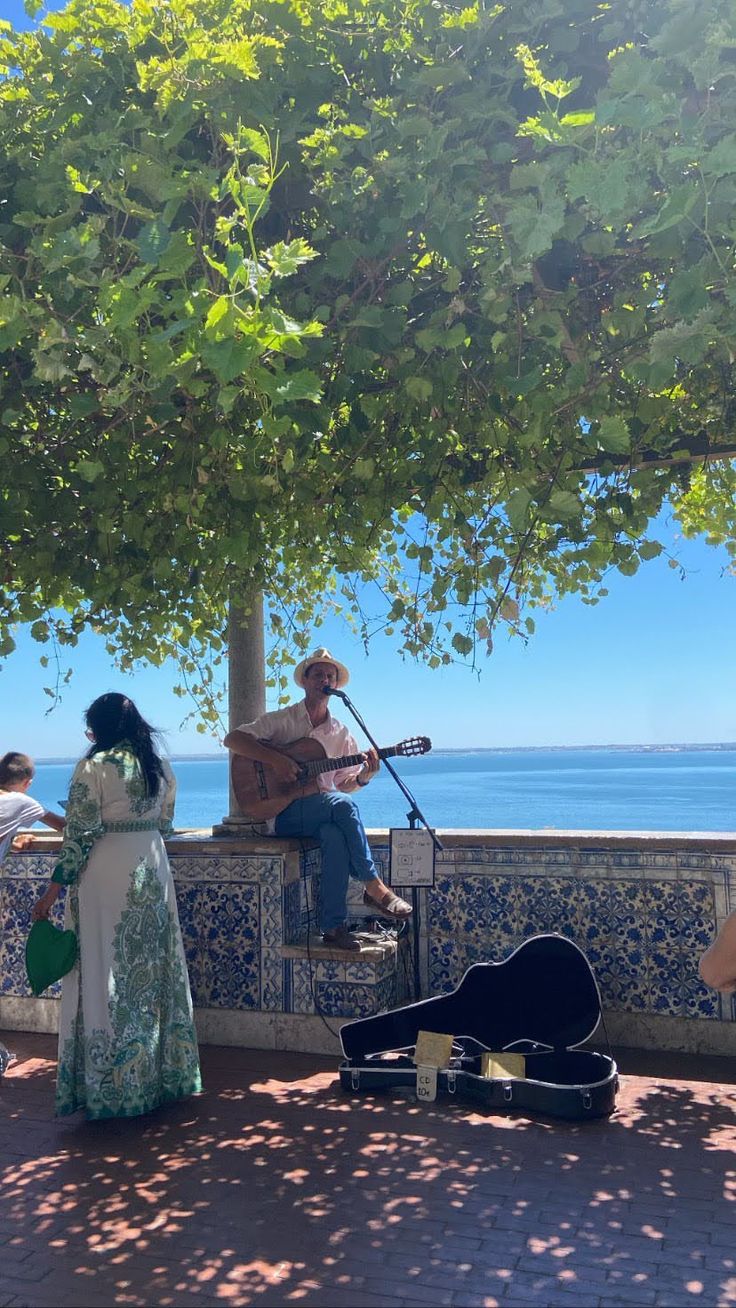 two people playing music under a tree near the water