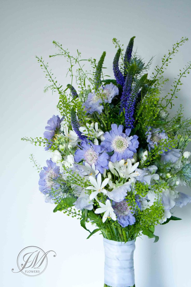 a bouquet of blue and white flowers in a vase with greenery on the side