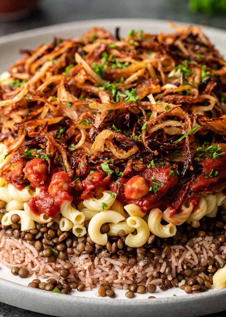 a white plate topped with pasta and meat covered in sauce on top of brown rice