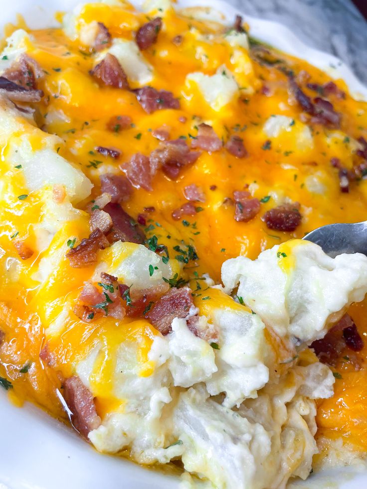 a white plate topped with mashed potatoes covered in cheese and bacon next to a fork