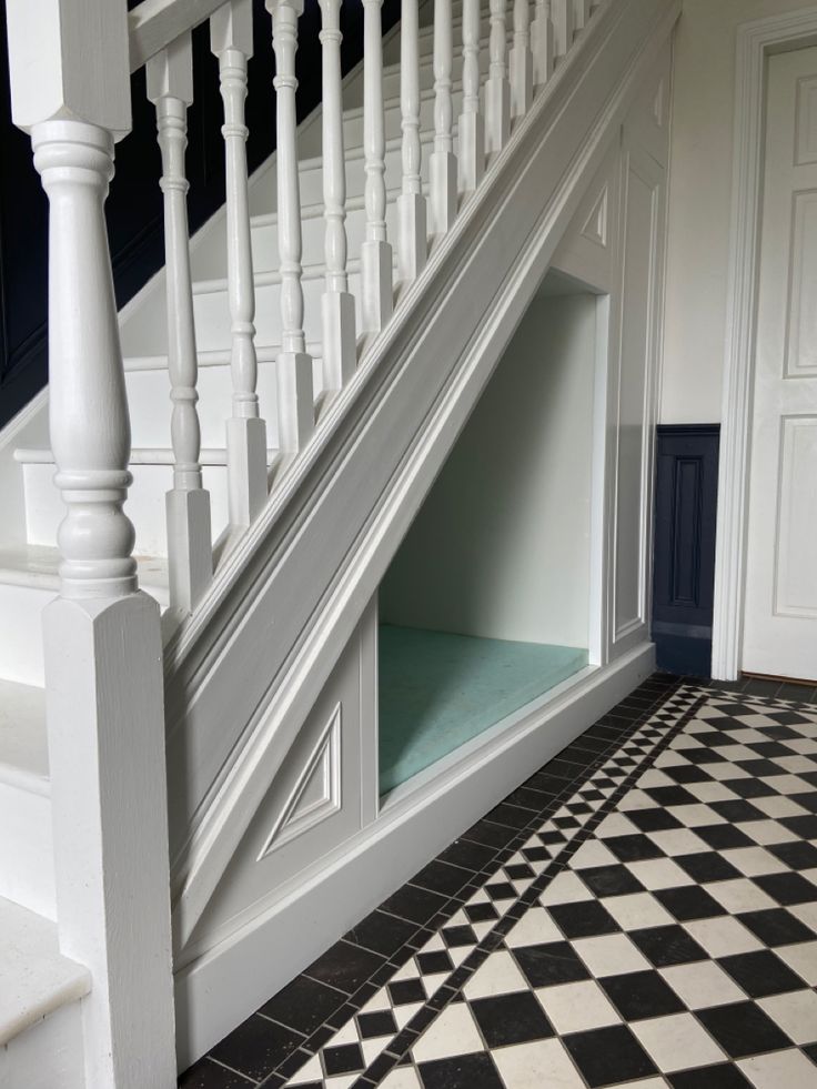 an open dog house under the stairs with black and white checkered tile flooring