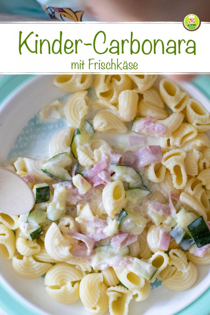 a white plate topped with pasta covered in ham and cheese next to a wooden spoon