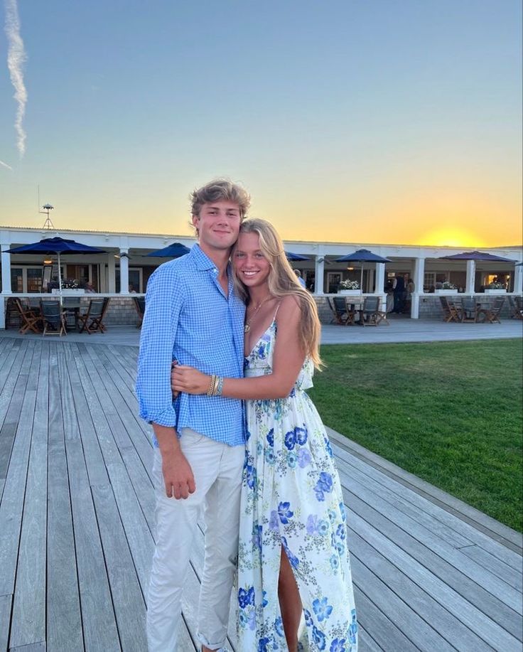 a man and woman posing for a photo on a deck with the sun setting in the background