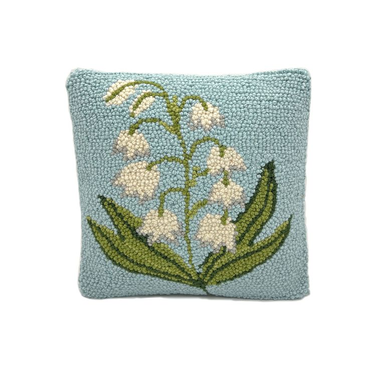 a blue pillow with white flowers and green leaves on the front, sitting on a white surface