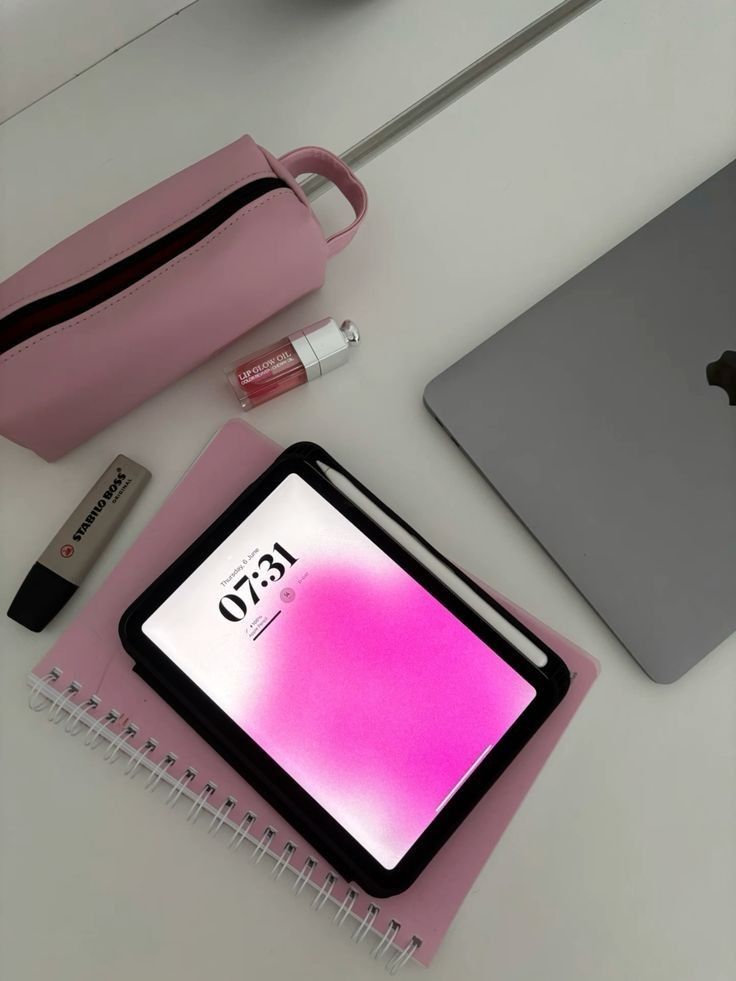 an apple laptop computer sitting on top of a desk next to a pink bag and pen