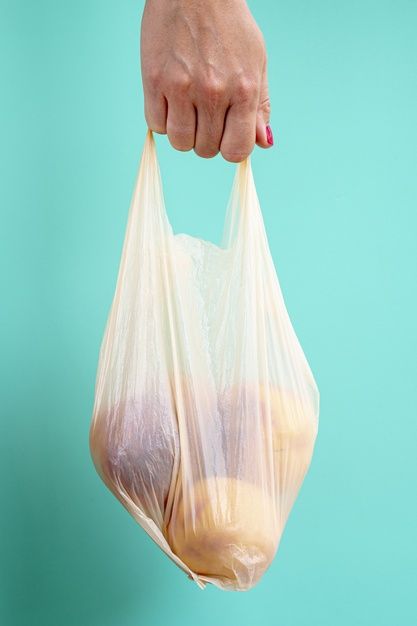 a person's hand holding a plastic bag filled with food on a blue background