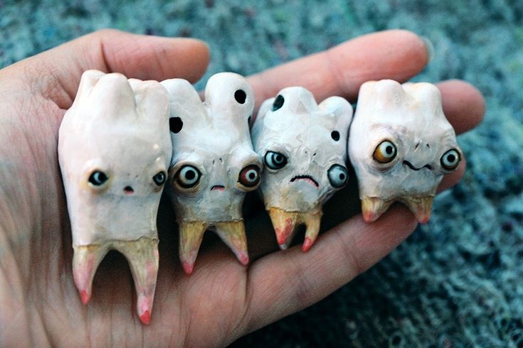 a hand holding five fake teeth with eyes on them