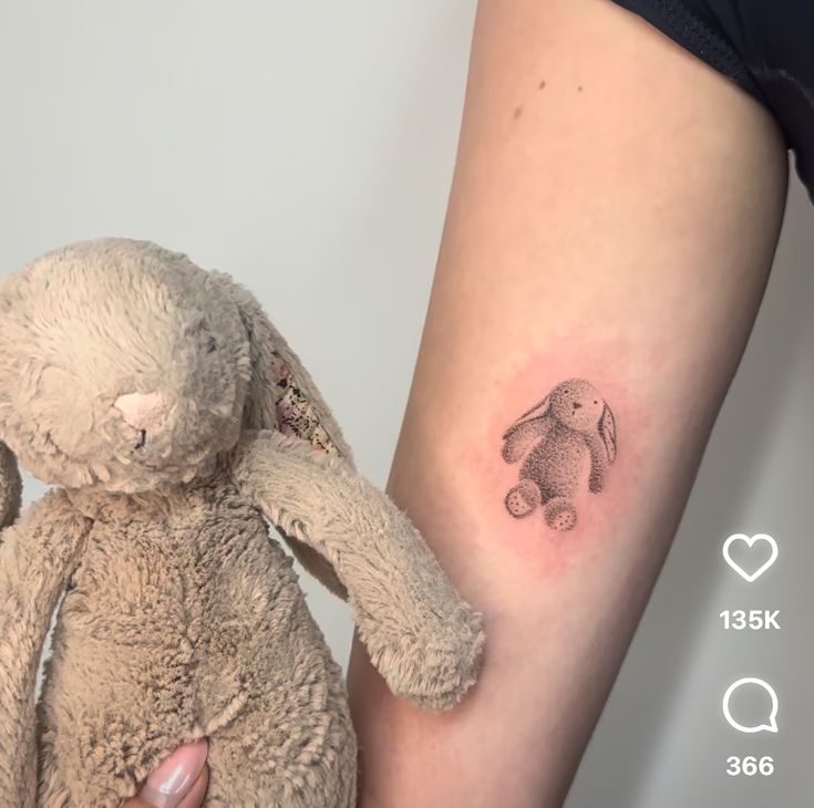 a small tattoo on the arm of a girl with a teddy bear next to her