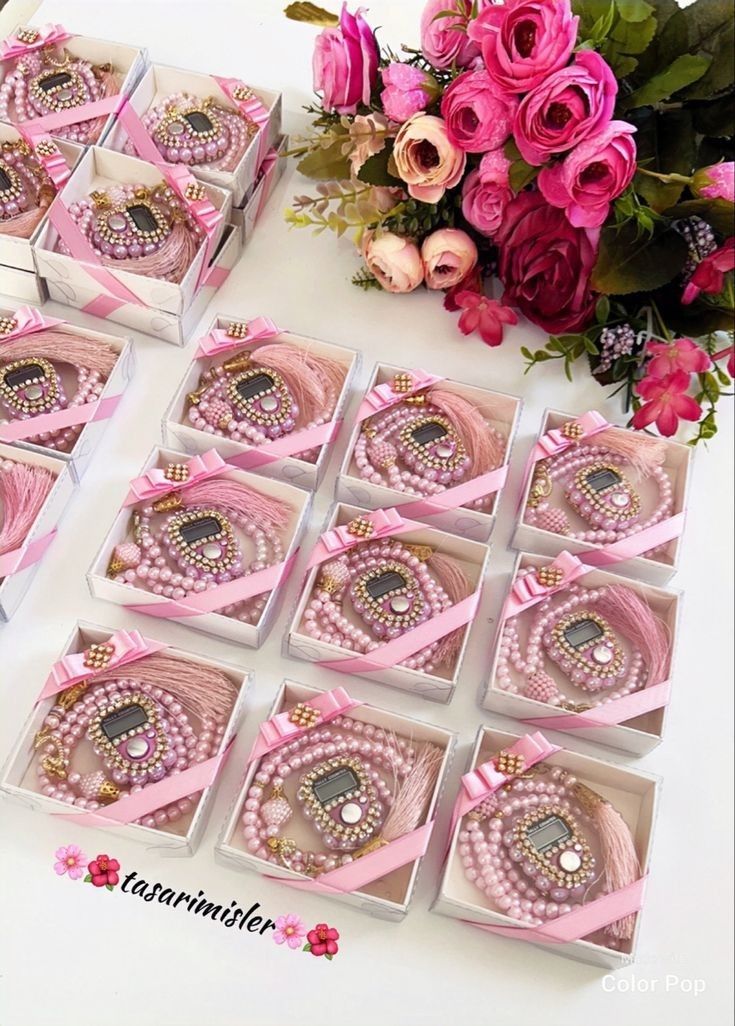 several pink bracelets in boxes on a table next to flowers and roses with ribbons