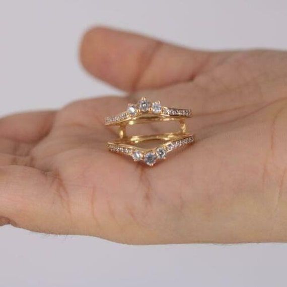 a person's hand holding a gold ring with three diamonds on top and bottom