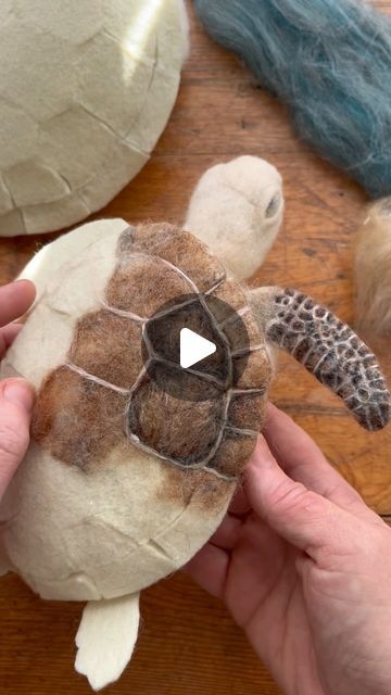 someone is holding a turtle made out of toilet paper and yarn on a wooden table