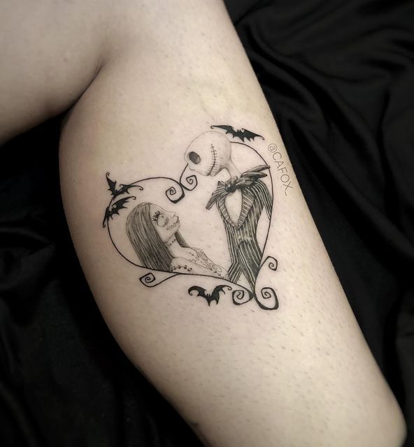 a couple in a heart shaped frame tattoo on the left thigh, with bats flying around