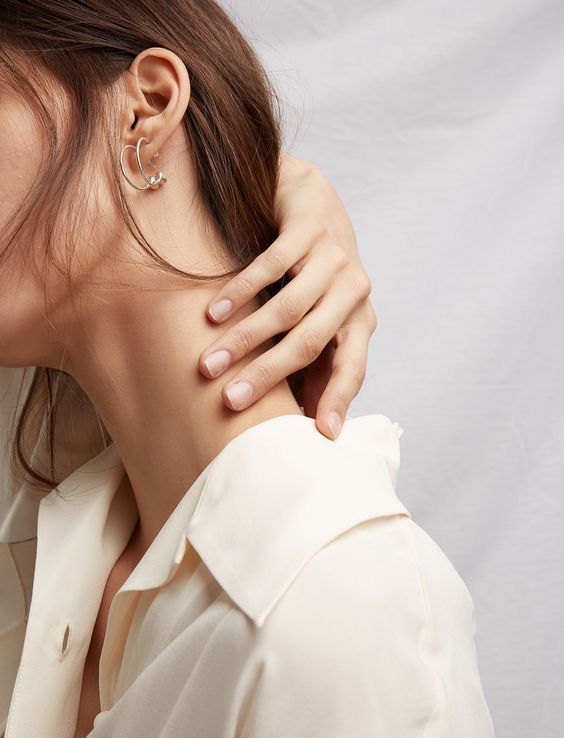 a woman with her hand on the back of her neck, wearing a white shirt