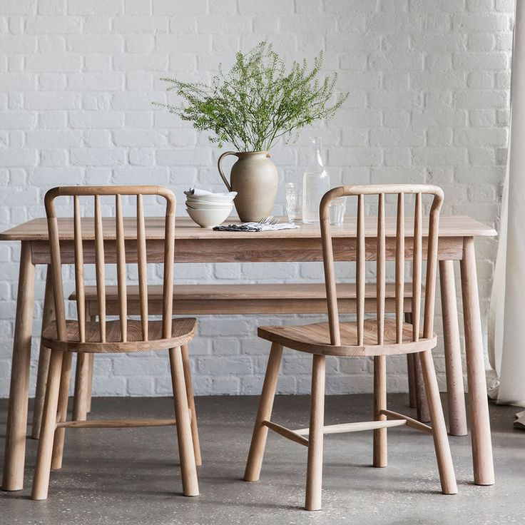 two wooden chairs and a table in front of a white brick wall with a potted plant on it